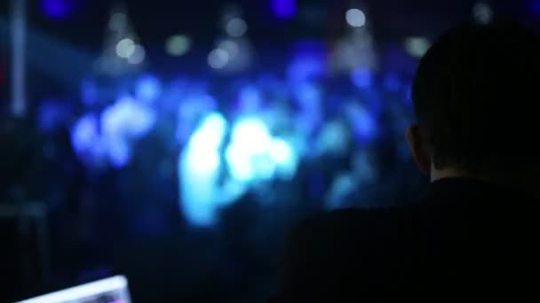 Primer plano de una vista de la cabeza del DJ por detrás, y en un fondo borroso la gente bokeh bailar en una fiesta. DJ trabajando en una fiesta . — Vídeo de stock