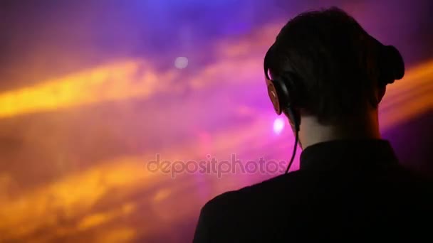 Vista trasera. La espalda y los auriculares del DJ en primer plano, la gente bailando son borrosas . — Vídeos de Stock