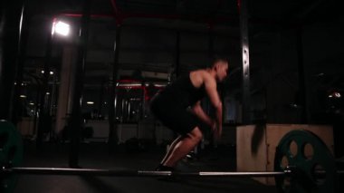 Yakın çekim, kamera hedefin arkasından hareket ediyor. Bir dairesel kardiyo egzersiz egzersizler, bir dizi için tasarlanmış siyah T-shirt bir adam ve siyah pantolon, boppy ahşap bir küp üzerinde atlama ile gerçekleştirir