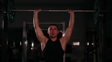 Siyah giysili atlet bar başının üzerinde bir ağırlık ile dinamik bir hızda iter. Onu izleyen ve enine üzerinde yukarı çekerek turnike için gelir.