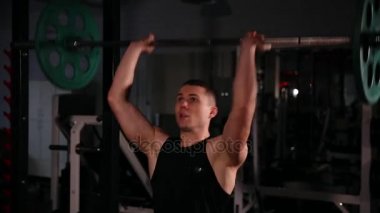 Siyah giysili atlet bar başının üzerinde bir ağırlık ile dinamik bir hızda iter. Turnike için geliyor, bu izler ve enine üzerinde güç çıkışını gerçekleştirir.