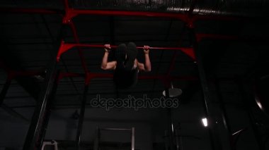 Atlet spor salonunda siyah giysili bir elektrik prizine takın yatay çubuk üzerinde gerçekleştirir. Aşağıdan bir geniş açılı görünüş.