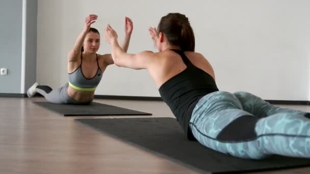 Deux filles dans la salle de gym en vêtements de sport tout en étant l'un l'autre amis effectuer l'exercice de superman dans un balancement dynamique sur le ventre. Vue latérale gros plan . — Video