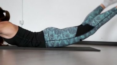 Yüzleri karşı karşıya Spor paspaslar üzerine yalan bir egzersiz Süpermen performans spor giyim'de iki güzel kız close-up. Kamera vücut hareketleri.