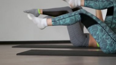 Salonun üzerinde yalan pilates egzersiz sırasında spor salonunda dönüşümlü olarak onların arkasında yatan paspaslar iki kız dizlerinin uyluk kasları germe göğüs çek. Zaman uyumlu yürütülmesi