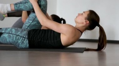 Salonun üzerinde yalan pilates egzersiz sırasında spor salonunda dönüşümlü olarak onların arkasında yatan paspaslar iki kız dizlerinin uyluk kasları germe göğüs çek. Zaman uyumlu yürütülmesi