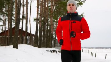 Bir koşucu kırmızı ceketli casual giyim Jumper'la ormanda yoluyla çalışır. Büyük bir atlet kameraya benziyor. Ağır çekim. 120 kare / saniye