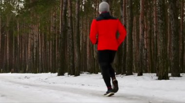 Kırmızı ceketli genç bir adam olarak bir jumper casual giyim orman yoluyla çalışır. Arkadan Görünüm. Ağır çekim. 120 kare / saniye