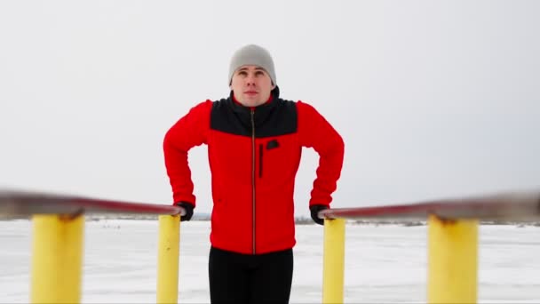 Een sport opgeleide man voert push-ups op parallelle staven in de winter in de open lucht. — Stockvideo