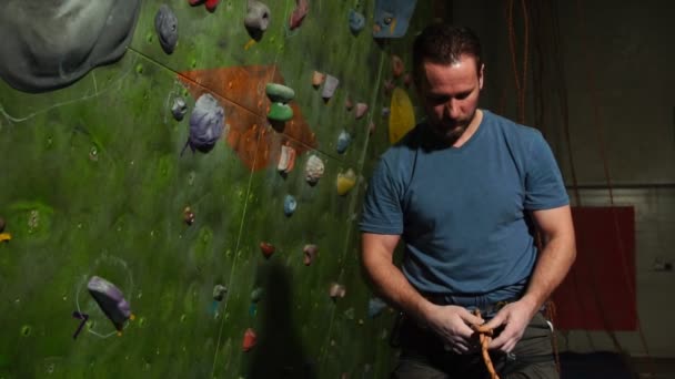 Ένας ορειβάτης άνθρωπος προετοιμάζει τον εξοπλισμό με φόντο έναν τοίχο αναρρίχησης. Δεμένη κόμπο για αναρρίχηση ενός βουνού. Αργή κίνηση. — Αρχείο Βίντεο