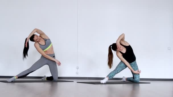 Две красивые девушки выполняют склоны в стороне на коленях, упражнения для пилатеса — стоковое видео
