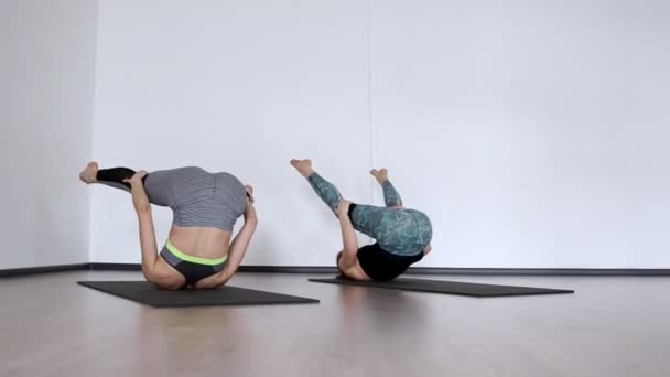 Twee meisjes in de sportschool uitvoeren een oefening klubochalka Pilatus hassel. Lezhnaya op haar rug met haar benen verhoogd maken een roll op haar rug. de camera gaat in een baan — Stockvideo