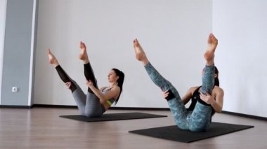 İki kız spor salonunda bir egzersiz klubochalka gerçekleştirin. Pilate hassel. Lezhnaya bacaklarını kaldırdı ile sırtında sırtında bir rulo yapın. kamera yörüngede hareket ediyor. Beyaz bir egzersiz yapıyor