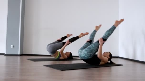 Duas meninas no ginásio realizar um exercício klubochalka. Hassel de Pilatos. Lezhnaya em suas costas com as pernas levantadas fazer um rolo em suas costas. A câmara está em órbita. Fazendo exercício em um branco — Vídeo de Stock