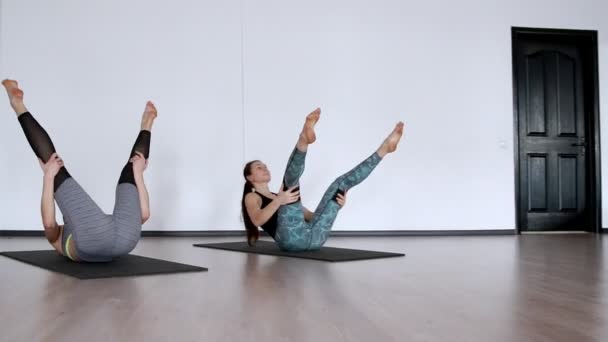 Twee meisjes in de sportschool uitvoeren een oefening klubochalka Pilatus hassel. Lezhnaya op haar rug met haar benen verhoogd maken een roll op haar rug. de camera gaat in een baan. Doen oefening op een wit — Stockvideo