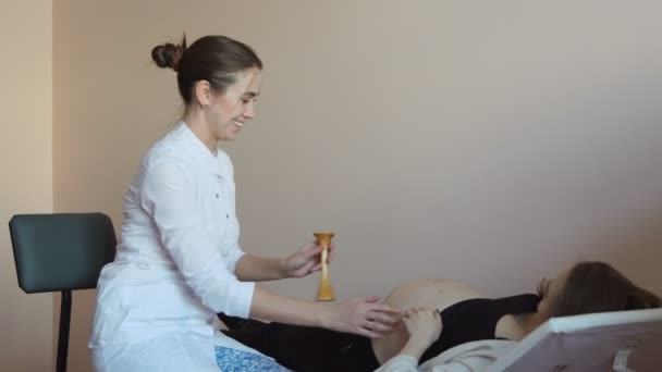 Těhotná žena leží na gauči v klinice a ženský lékař poslouchá babys puls přes břicho za pomoci sluchové doppler — Stock video