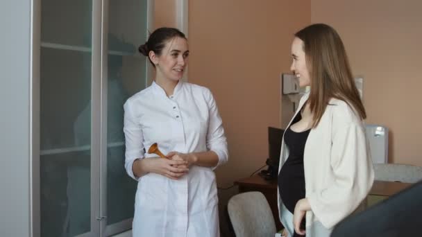 A female doctor and a young pregnant woman are standing in the office and talking about motherhood. — Stock Video