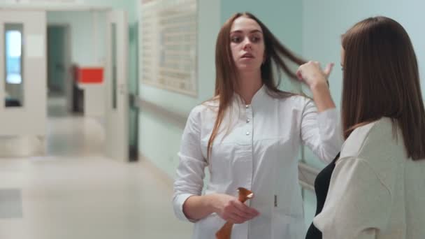 Een zwangere vrouw die permanent in de gang van de transplantatie centrum communiceert met een dokter in een witte badjas. Voorbereiding voor de bevalling. baby in de maag. — Stockvideo