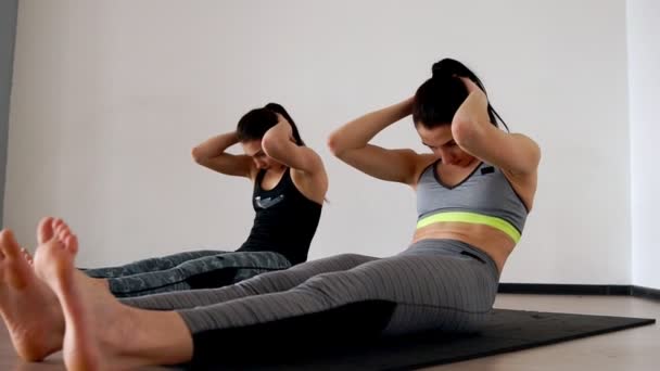 Twee vrouwen close-up crunches liggend op je rug doen crunches met been werpt. Het algemeen plan van de camera beweegt langs het lichaam. — Stockvideo