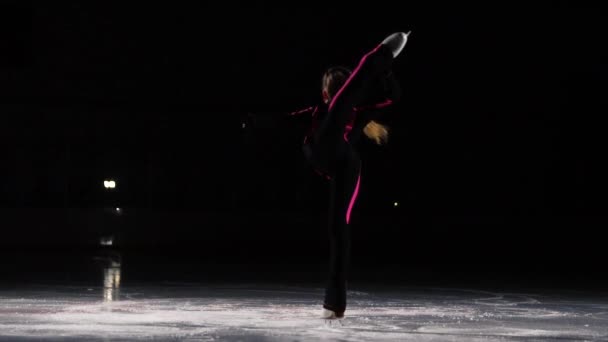 Mała dziewczyna skater w sporty czarny garnitur i białą rolki wykonuje podstawka przędzenia w hali lodowiska. Stojąc na jednej nodze do przytrzymaj tarczę z dłoni. Łyżwiarka figurowa — Wideo stockowe