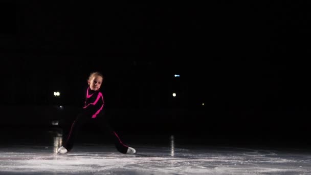 Mała dziewczyna skater w sporty czarny garnitur i białą rolki wykonuje podstawka przędzenia w hali lodowiska. — Wideo stockowe