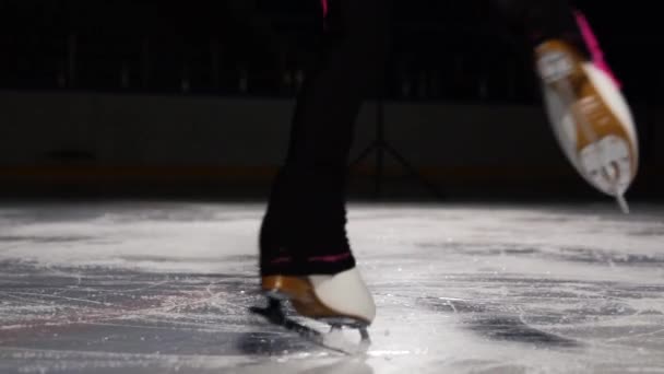 A professional skater performs a skating jump with the rotation in the air on the ice. Little girl portmian at competitions in figure skating. Close-up on a dark background. — Stock Video