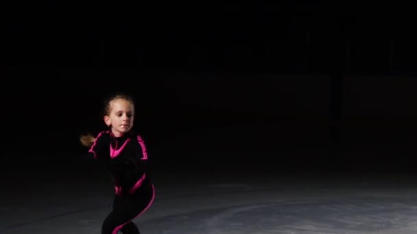 Una niña pequeña toma un patinaje futurista en la arena de hielo realizando un salto con rotación. La cámara se mueve detrás de ella. . — Vídeos de Stock