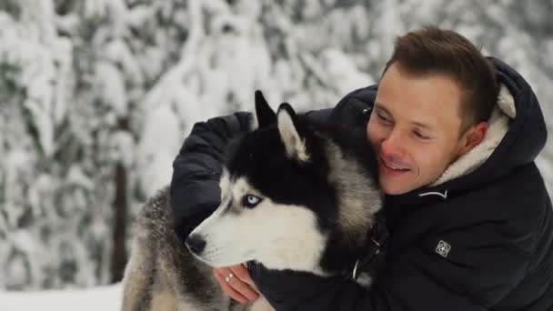 A man hugs his Siberian husky in the forest. In the background trees in the snow. Pride and happiness in the eyes. Walk with the dog. — Stock Video