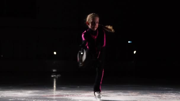 Una pequeña patinadora profesional en las competiciones de patinaje artístico realiza una rotación desde la posición sentada levantándose gradualmente en una pierna mientras sostiene la otra pierna con la mano detrás de la — Vídeo de stock