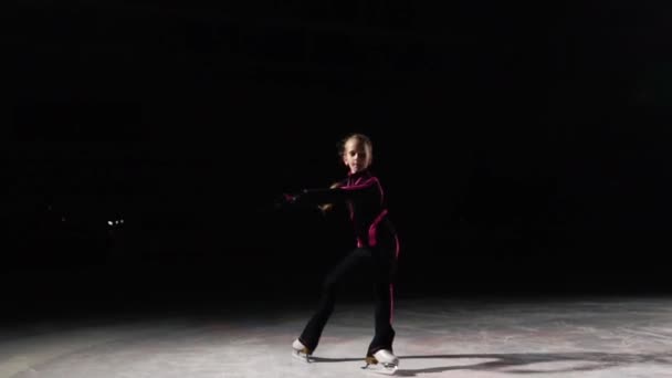 Uma patinadora profissional se move em um círculo no gelo em patins na posição quando os pés são implantados para os lados, e a câmera se move junto com ele. Patinação profissional atrasada. Luz de fundo — Vídeo de Stock