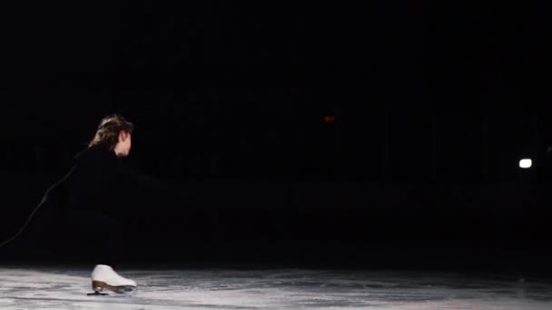 A professional skater in a black suit performs the rotation standing on one leg in a swallow position on ice in ice skates in a slow-motion shot. Camel spin — Stock Video