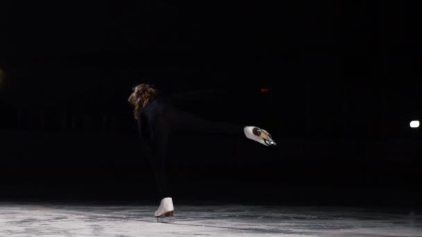 Un patinador profesional en traje negro realiza la rotación de pie sobre una pierna en posición de golondrina sobre hielo en patines de hielo en una toma en cámara lenta. Desde la posición de pie, cae en una sesión — Vídeos de Stock