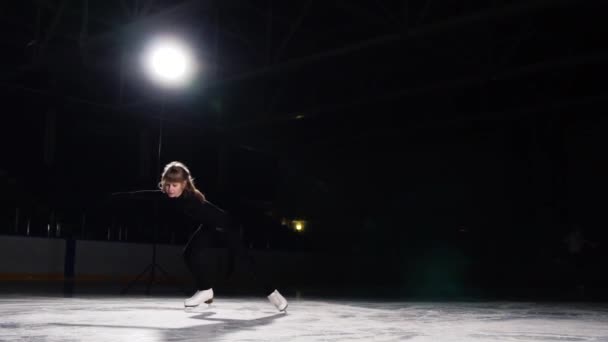 Une patineuse artistique professionnelle effectue du patinage avec un tour pour faire tourner une toupie avec son axe sur un fond noir . — Video