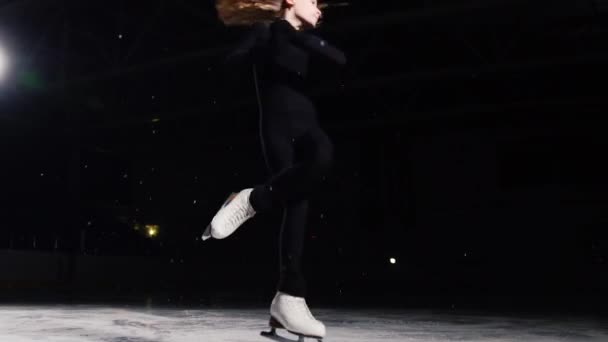 Een professioneel kunstschaatser voert schaatsen met een sprong in de lucht met een zwarte achtergrond in een zwart pak. — Stockvideo