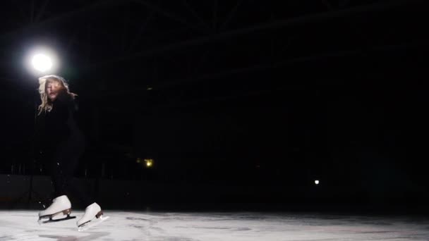Ein professioneller Eiskunstläufer macht Eislaufen mit einem Sprung in die Luft vor schwarzem Hintergrund im schwarzen Anzug. Zeitlupe. — Stockvideo
