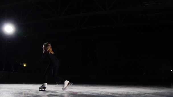 En professionell konståkare utför skridskoåkning med ett hopp i luften med en svart bakgrund i en svart kostym. Slow motion. — Stockvideo