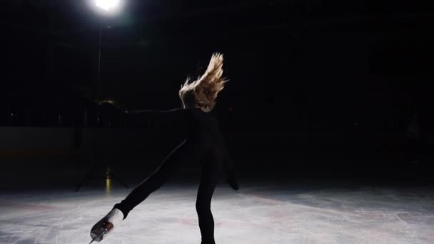 Uma mulher profissional, patinadora artística de um terno preto nas competições de patinação artística, realiza uma tripla revolução em torno de seu eixo no salto. E termina o programa com um arco. A câmera se move — Vídeo de Stock