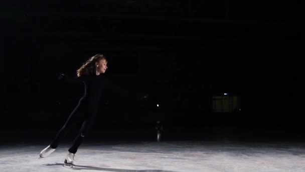 Ein professioneller Eiskunstläufer macht Eislaufen mit einem Sprung in die Luft vor schwarzem Hintergrund im schwarzen Anzug. Eisarena — Stockvideo