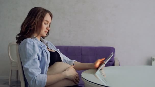 마시는 커피와 태블릿 컴퓨터를 사용 하 여 유리 식탁에 앉아 행복 한 임신 여자. 인터넷 비즈니스에 종사. 원격 작업은 출산 휴가에. 온라인 비디오 회의 — 비디오