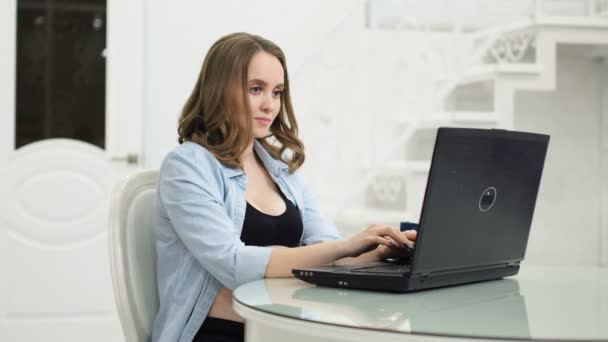 Uma mulher grávida escreve em um fórum mães com seu laptop sentado em uma mesa de vidro . — Vídeo de Stock