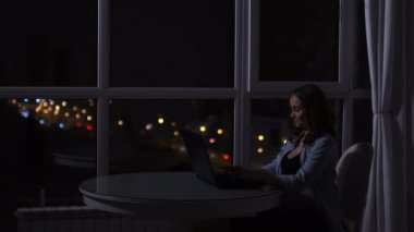 Hamile bir kadın geç saatlere kadar bilgisayarda çalışır. Bilgisayar büyük bir pencere önünde şehir manzaralı geceleri oturup gece.
