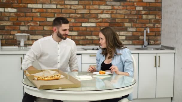 Uomo e donna incinta mangiano pizza a casa nella loro cucina. Una cattiva dieta. Cibi grassi. Obesità — Video Stock