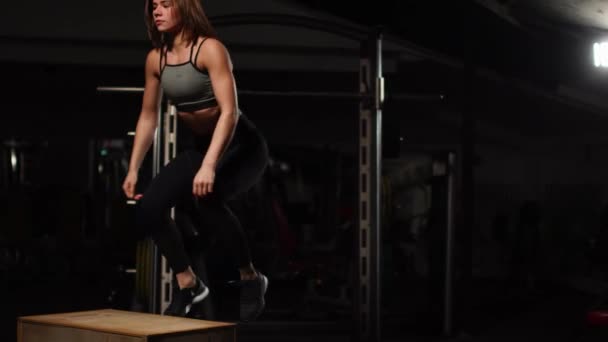 Vackra kvinnliga fitness idrottsman utför hopp låda i ett mörkt gym som bär svart sport topp och korta tights med ansiktet dolt — Stockvideo