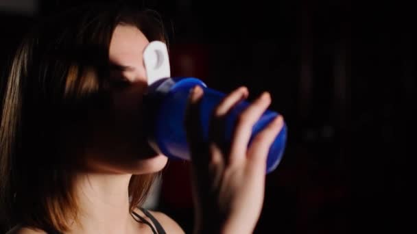Gorgeous νεαρή γυναίκα με μια πετσέτα για το λαιμό πόσιμο νερό από ένα μπουκάλι στο γυμναστήριο. — Αρχείο Βίντεο