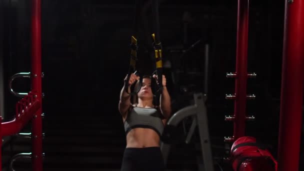 Young fit woman doing pull-ups on gymnastic rings. Muscular young female athlete exercising with rings at gym. — Stock Video