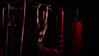 Güzel bir kadın açık bir karın ile siyah top bir pull-up çeker. Taşınabilir bir hall ile bir tempo arka plan üzerinde. Kız boksör. Sporcu eğitim.