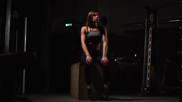 美丽的女性健身运动员表演方块跳跃在黑暗的健身房穿着黑色运动顶部和短紧身衣与脸隐藏 — 图库视频影像