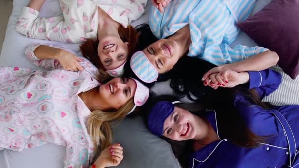 Čtyři ženy v pyžamu leží na posteli a podívat se přímo do kamery na pyžama party. — Stock video