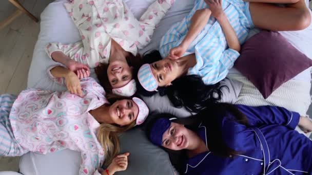 Vier lächelnde Frauen im Schlafanzug liegen auf dem Bett und blicken direkt in die Kamera einer Pyjama-Party. Brautjungfer. Junggeselle. fröhlich und fröhlich. — Stockvideo