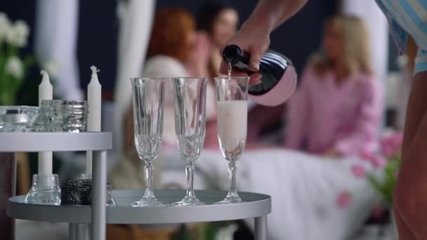 Gros plan d'une belle fille remplit de verres de champagne pour les copines qui s'amusent en arrière-plan lors d'une fête de célibataire . — Video